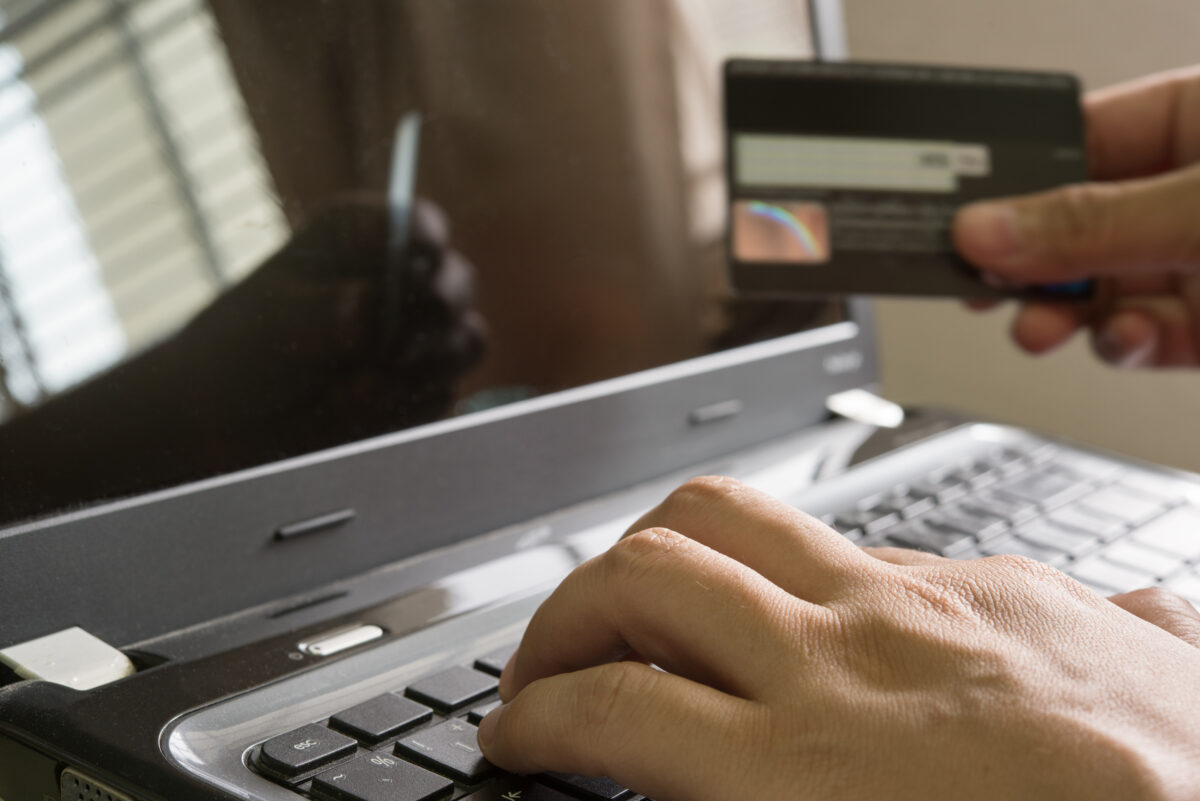Hand holding a credit card and using laptop